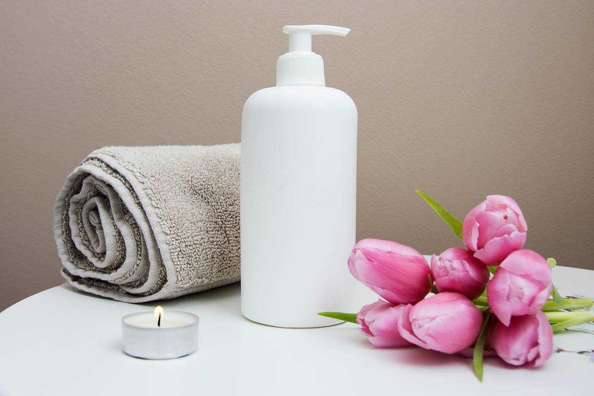 Woman holding bottle of bath body shower gel while examining ingredients label in bathroom